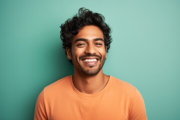 Obraz premium Portrait of a smiling indian man in his 20s smiling at the camera on solid pastel color wall