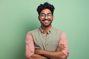 Fototapeta premium Portrait of a grinning indian man in his 20s with arms crossed in solid pastel color wall