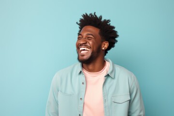 Fototapeta premium Portrait of a joyful afro-american man in his 20s laughing in solid pastel color wall