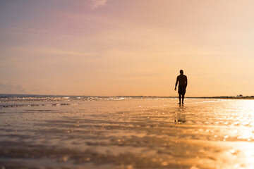 The silhouette of a man waking along the seashore at sunset