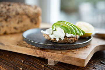 Fresh avocado slices on grain bread with cream cheese and lemon. Vegetarian food on wooden cutting...