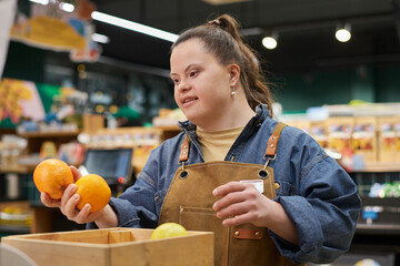 Waist up portrait of smiling young woman with disability working in supermarket sorting fresh...