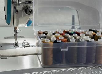 Close-up of a box with spools of thread of different colors standing near a sewing machine for...