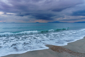 ocean with blue waves and grey clouds on the beach during sunset