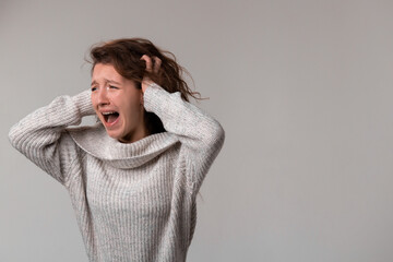 A woman in a sweater is screaming, clutching her hair in distress