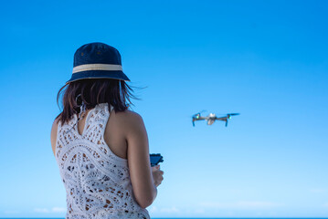 Asian woman controlling and flying a recreational drone at the beach to take pictures. Beautiful sunny day with blue sky.