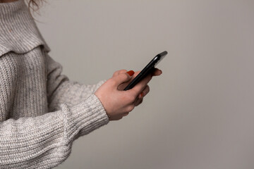 A woman in a sweater is holding a cell phone in her hand