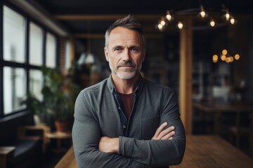 Naklejka premium Portrait of a glad man in his 50s with arms crossed while standing against scandinavian-style interior background