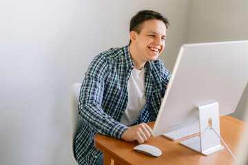 Portrait of happy freelancer man sitting at desk with laptop computer at home office, looking and smiling at screen