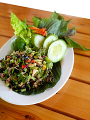 Traditional Laos Larb salad served with fresh cucumbers, lettuce, and herbs on a white plate over a wooden table