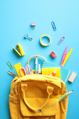 Yellow backpack filled with colorful school supplies on a bright blue background. Back to school...