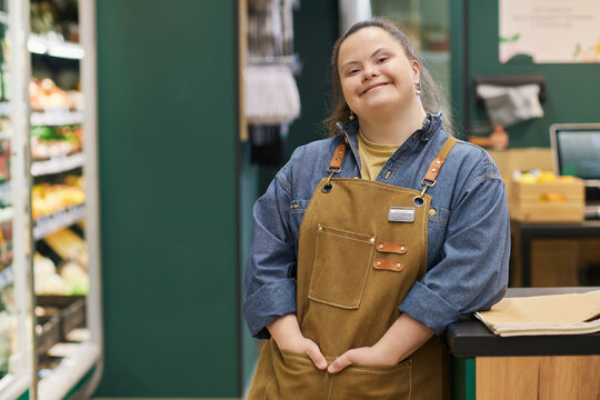 Waist up portrait of smiling young woman with Down syndrome enjoying work in supermarket and looking at camera with happiness copy space 