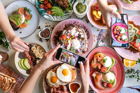Friends taking pictures of food on the table with smartphones during brunch in restaurant .