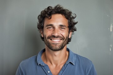 Fototapeta premium Portrait of a cheerful man in his 30s smiling at the camera in front of bare concrete or plaster wall