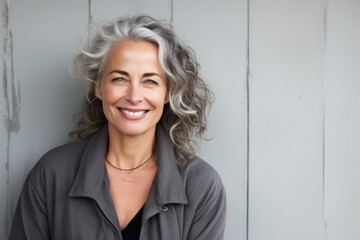 Portrait of a blissful woman in her 50s smiling at the camera over bare concrete or plaster wall
