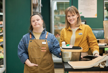 Waist up portrait of smiling manager and young woman with Down syndrome working in supermarket and...