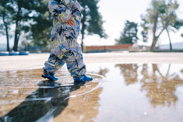 Small child in overalls walks through a puddle. Cropped. Faceless