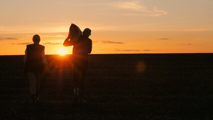 In the evening light, a man stands in a field with a bag on his shoulder, next to his wife, as the...