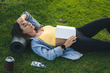 Brunette woman laying on the grass and falling asleep while she was reading a book.Tired after...