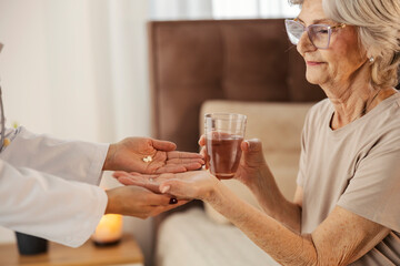 Close up of doctor's hands giving pills to a sick old woman during her home visit.