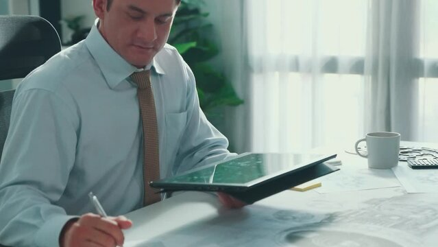 Professional engineer looking at phone while working on tablet with green screen at meeting table with turbine engine or jet engine sketch design and various metal gear scatter around. Alimentation.