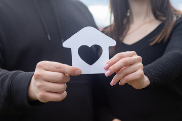 A young couple shows a house with a heart inside.