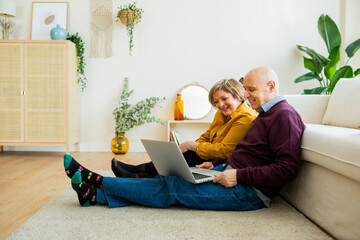 Senior couple having a video call on a laptop, both smiling at the screen. Senior couple sitting in a cozy living room, enjoying the moment and connecting with loved ones online.
