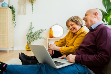 Senior couple having a video call on a laptop, both smiling at the screen. Senior couple sitting in a cozy living room, enjoying the moment and connecting with loved ones online.