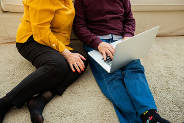 Senior couple sitting on the floor and using a laptop. Senior's hands using a computer in a comfortable home setting.