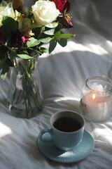 Flowers, coffee cups, and candle on a cozy bed