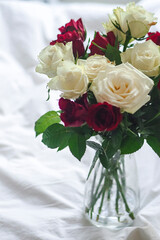 Vase filled with red and white roses on a bed