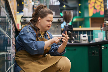 Side view portrait of independent young woman with Down syndrome working in cafe and using...