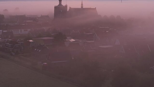 Aerial view of foggy sunrise over rooftops and windmill in historic Workum, Friesland, Netherlands.