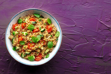 Quinoa tabbouleh salad in a bowl, a healthy dinner with tomatoes and mint, top shot with copy space on a purple background