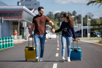 Couple leaving the airport hand in hand with their suitcases. Couple on honeymoon in their favorite...