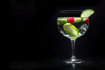 Fancy cocktail with fresh fruit. Gin and tonic drink with ice at a party, on a black background. Alcohol with lime and raspberry, with a place for text