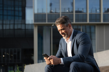 Confident middle age male entrepreneur businessman in formal suit working on mobile cell phone at office. Successful 40s mature hispanic senior business man using smartphone cellphone financial app - Powered by Adobe