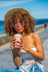 Stylish latin woman drinking iced juice next to the sea