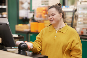 Waist up portrait of smiling young woman with Down syndrome using self checkout machine while...