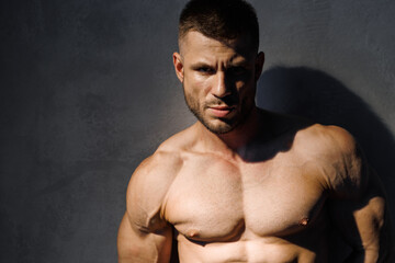 Fototapeta premium Muscular model sports young man on dark background. Fashion portrait of strong brutal guy. Male flexing his muscles.