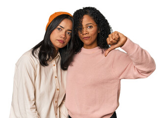 Young Latin friends together in studio showing a dislike gesture, thumbs down. Disagreement concept.