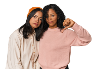 Young Latin friends together in studio showing a dislike gesture, thumbs down. Disagreement concept.