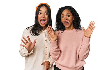 Young Latin friends together in studio receiving a pleasant surprise, excited and raising hands.