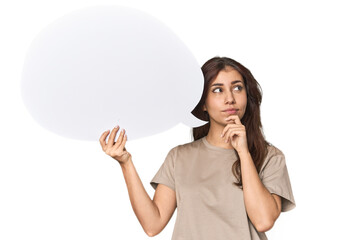 Middle Eastern woman holding comic bubble looking sideways with doubtful and skeptical expression.