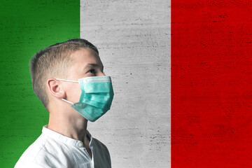 Boy in a medical mask on his face on background of Italy flag. Epidemic virus 2019-nCoV Respiratory...