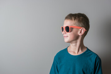Teenager boy in coral color sunglasses and blue t-shirt on bright background.