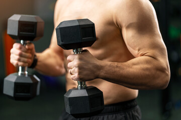Close up portrait of pumped up sexy man with muscular body holding dumbbells doing exercises in gym