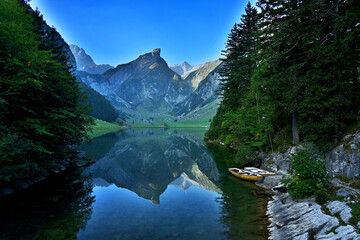 Zwei Ruderboote liegen am Ufer des idyllischen Seealpsee in der Schweiz und die Berge des Alpstein spiegeln sich im klaren und ruhigen Wasser des See