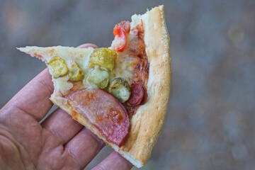 hand holding one piece of pepperoni pizza in the street