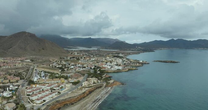 Aerial view of coastal town with sea, mountains, and homes, Cala Tabaco, Isla Plana, Murcia, Spain.